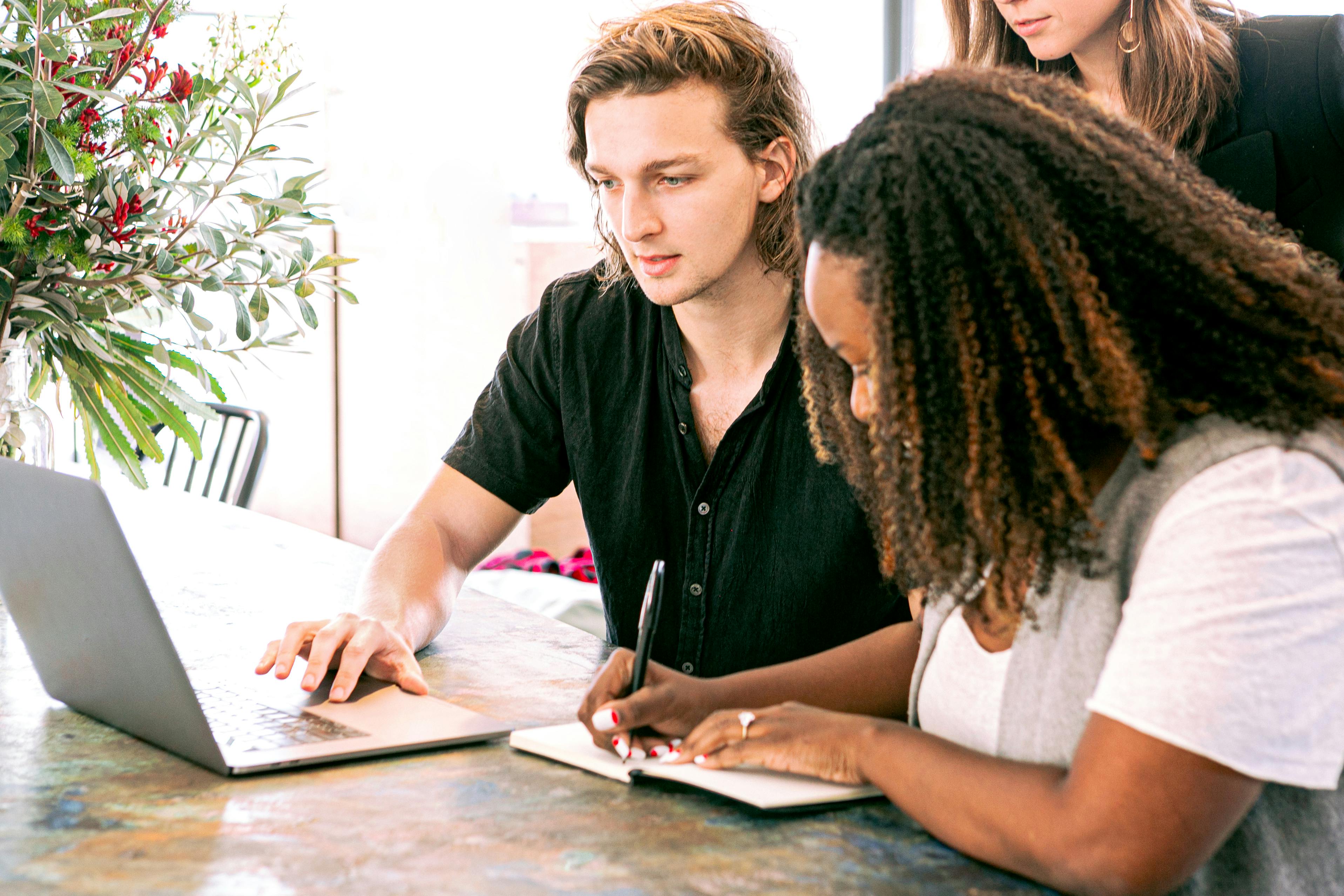 Man and woman looking at a laptop screen and taking notes