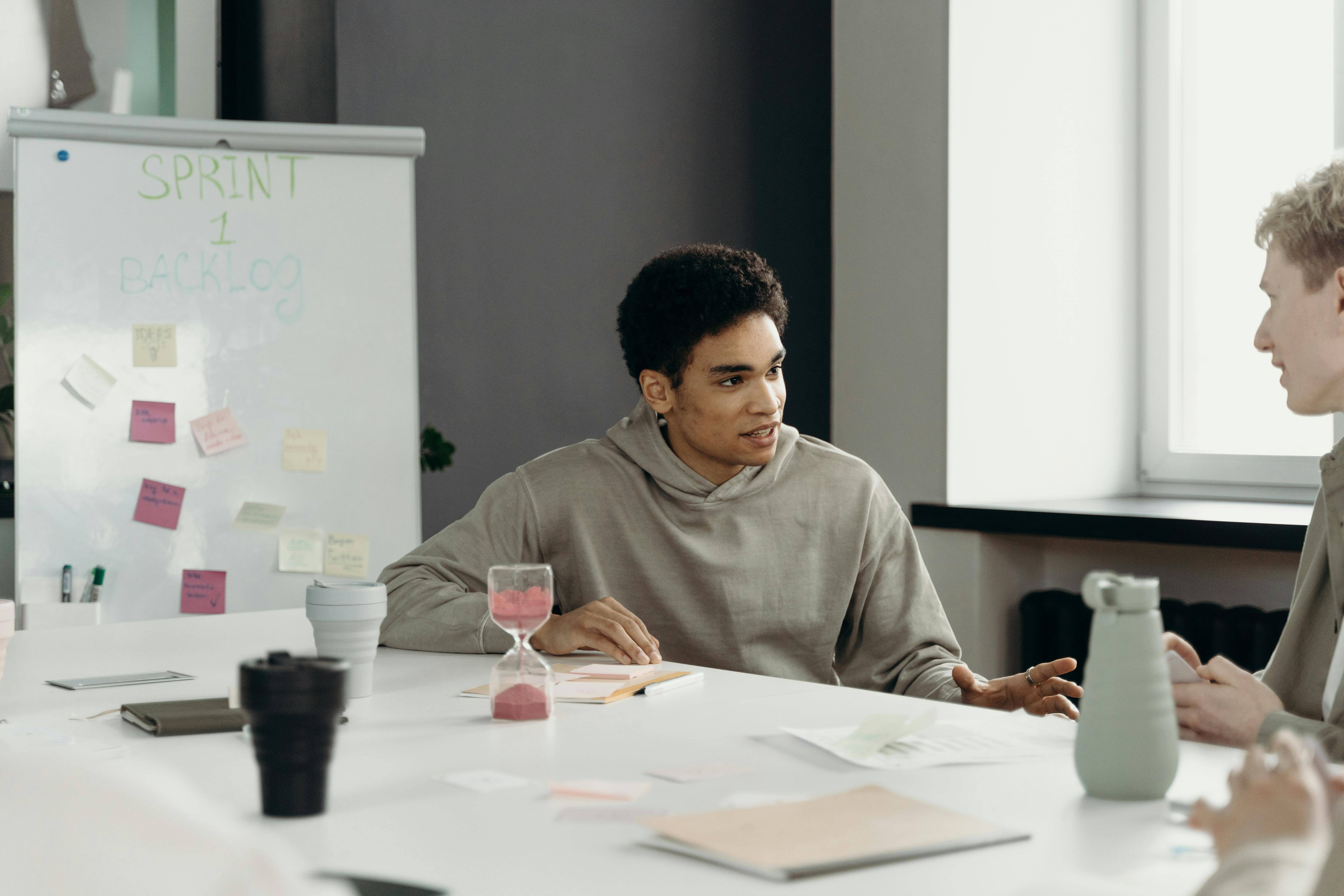 Two colleagues sat at a board desk with a sand timer and sticky notes on a white board