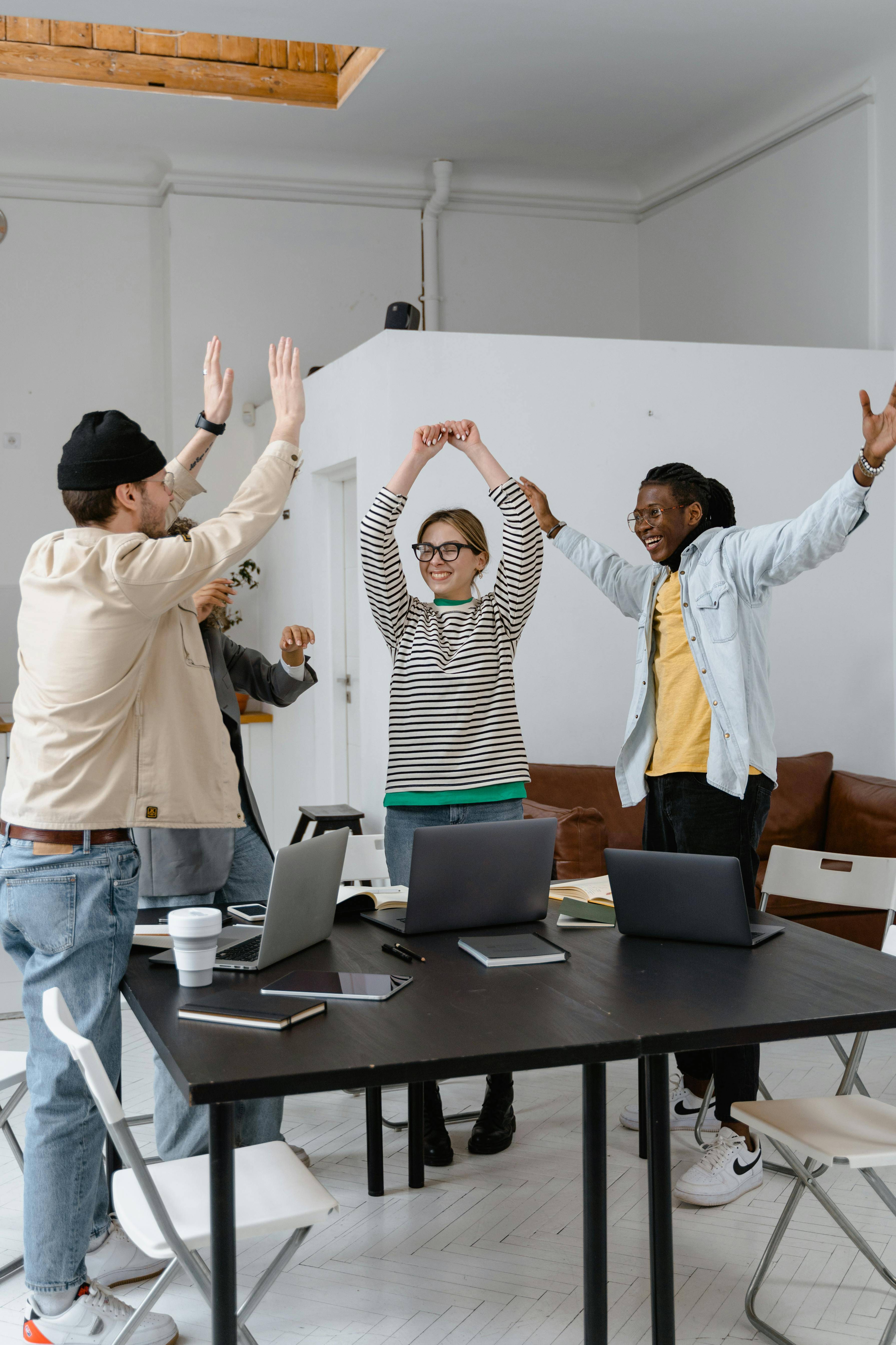 Happy colleagues with their arms in the air around a meeting desk