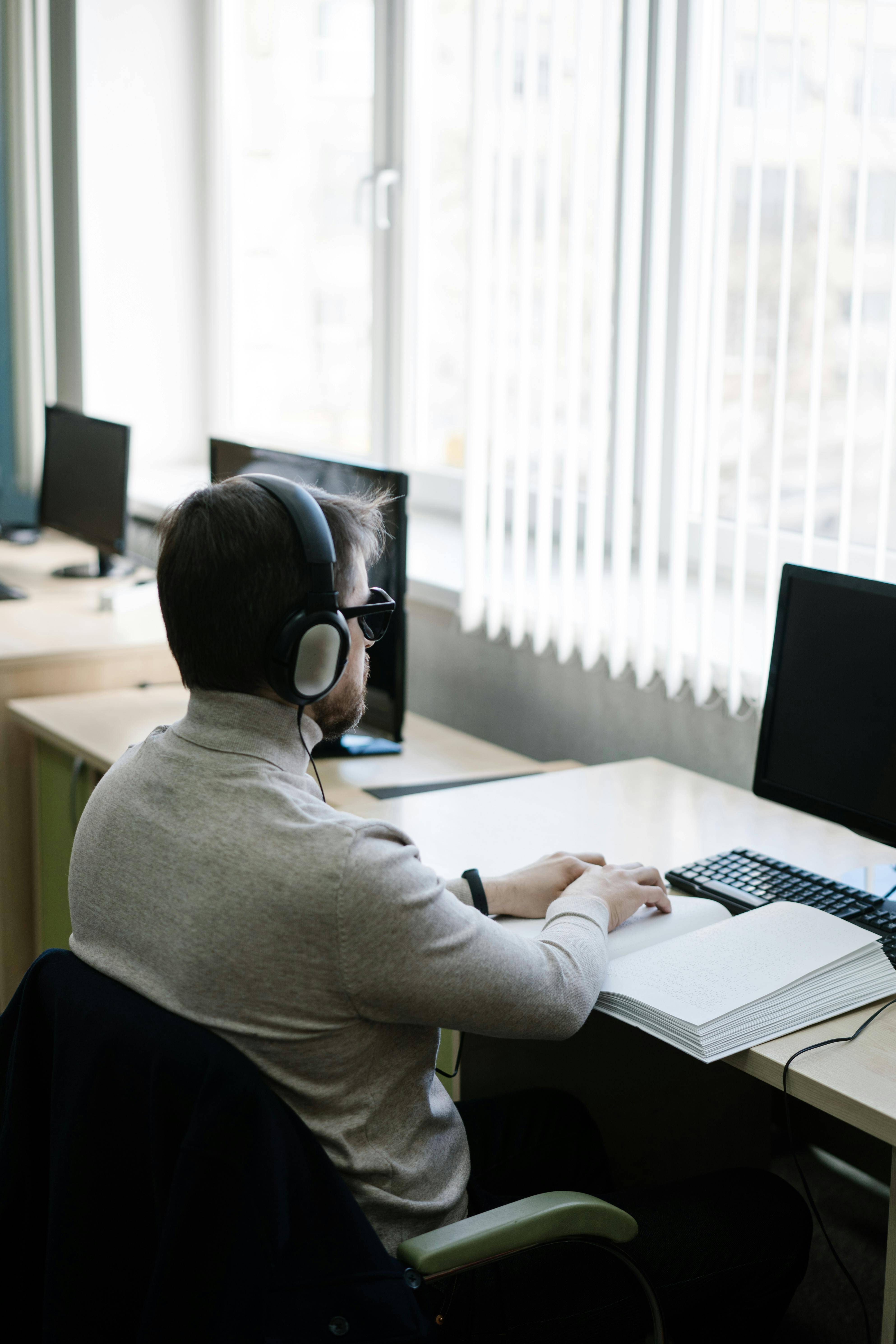 Blind man reading braille in a book wearing headphones